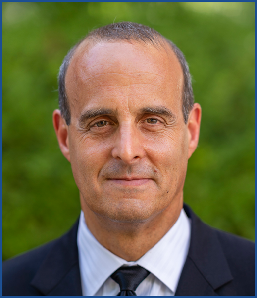 Headshot of a balding man wearing a navy blazer standing outside.